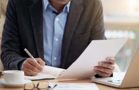 Cropped image of businessman reading document and writing ideas in notepad