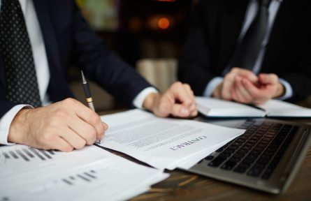 Closeup portrait of unrecognizable successful businessman wearing black formal suit reviewing documents and signing contract during meeting