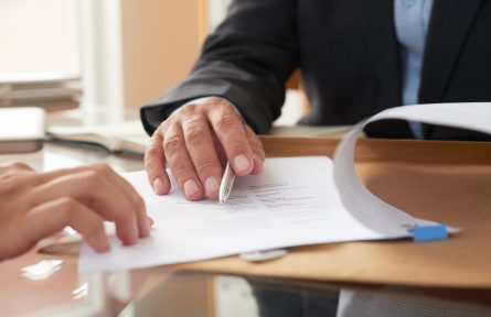 Close-up of businessman examining business contract and signing it at the office desk